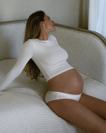 Pregnant woman reclining on sofa wearing white outfit